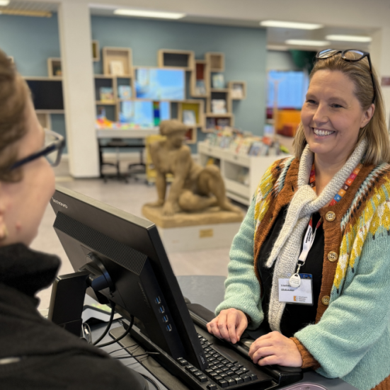 Foto af personalet på biblioteket der smiler mens de betjener en biblioteksbruger