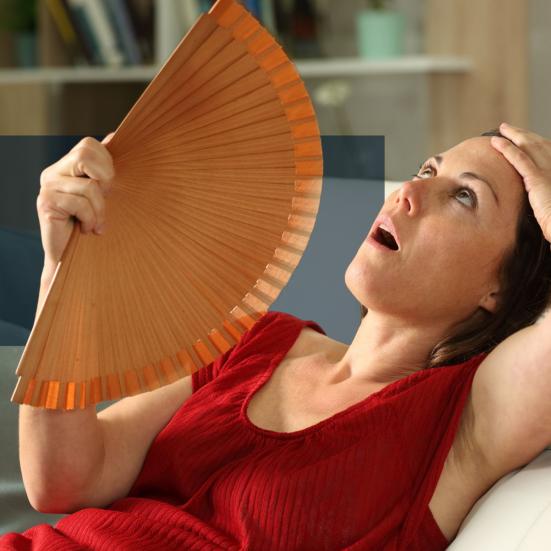 Kvinde, der sidder i en sofa og vifter sig med en håndvifte.