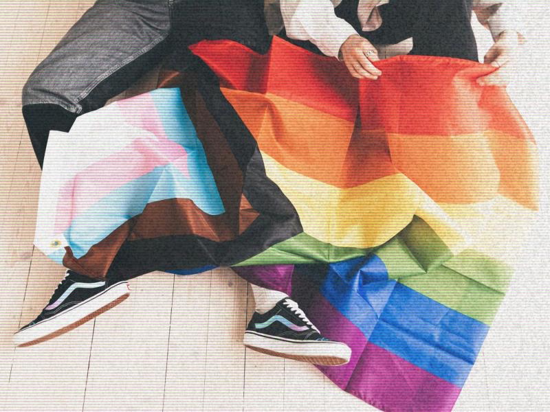 En person sidder med et Pride-flag viklet omkring sig; sneakers og flagets farver fylder billedet.