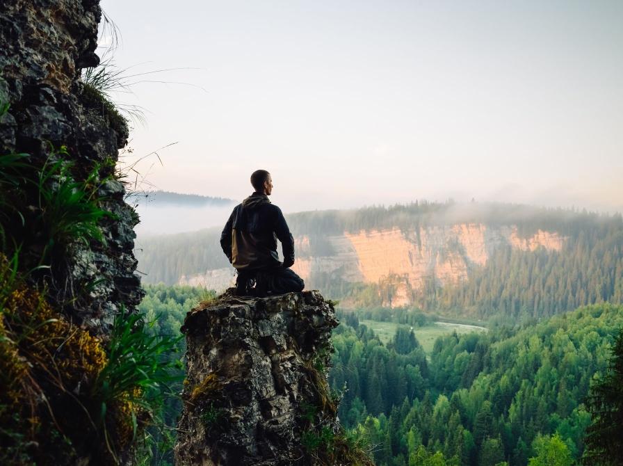 Mand sidder på sten og kigger ud over bjerge